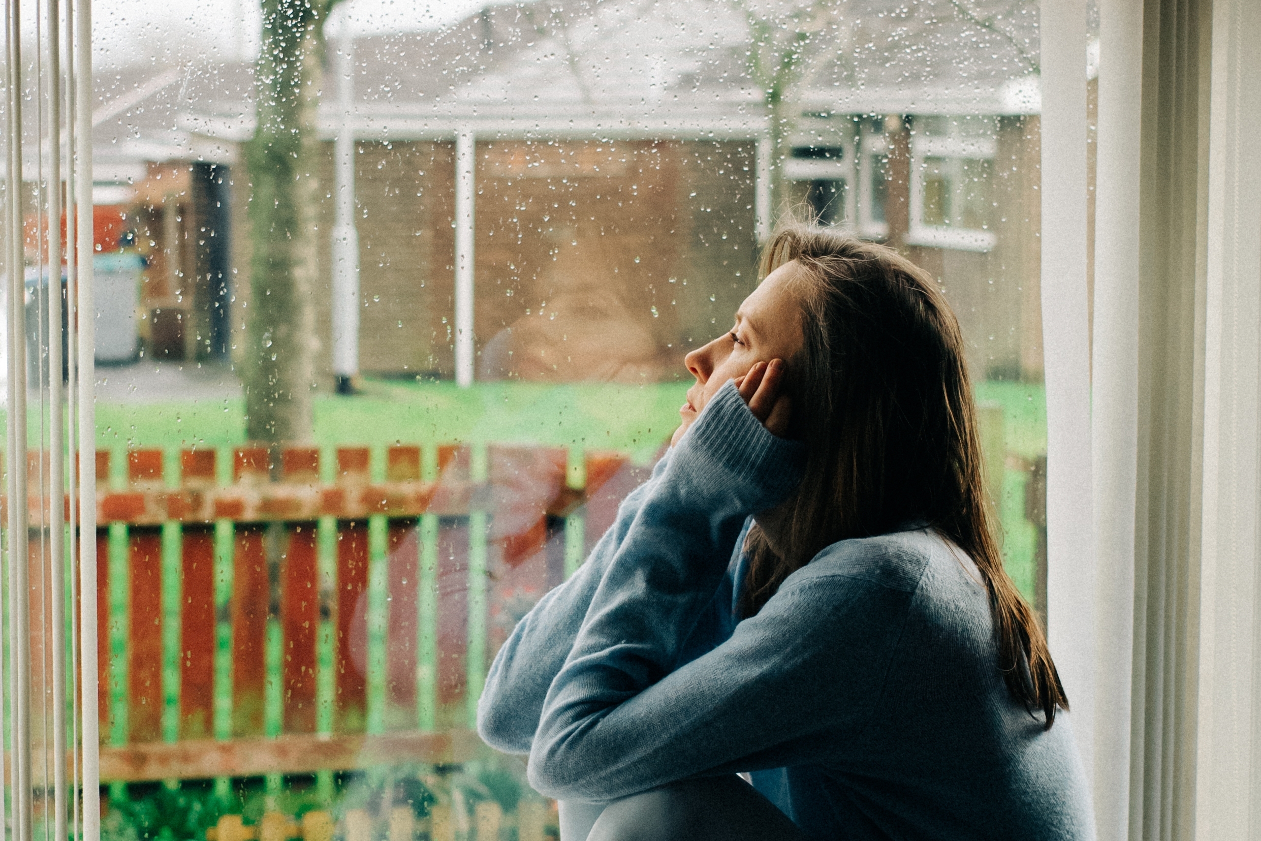 Woman looking out her window at the rain due to depression during the holidays