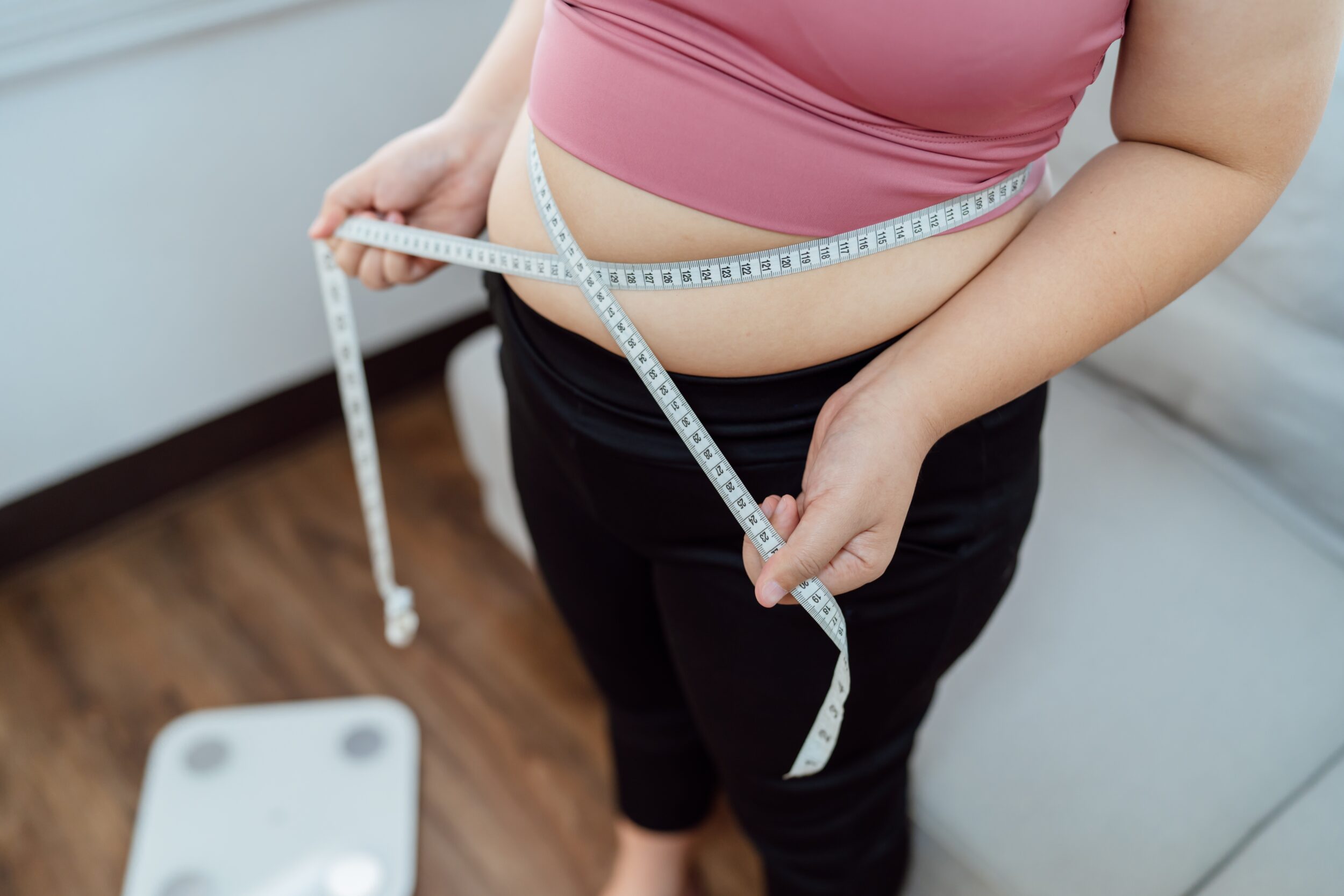 Overweight woman taking measurements of abdomen