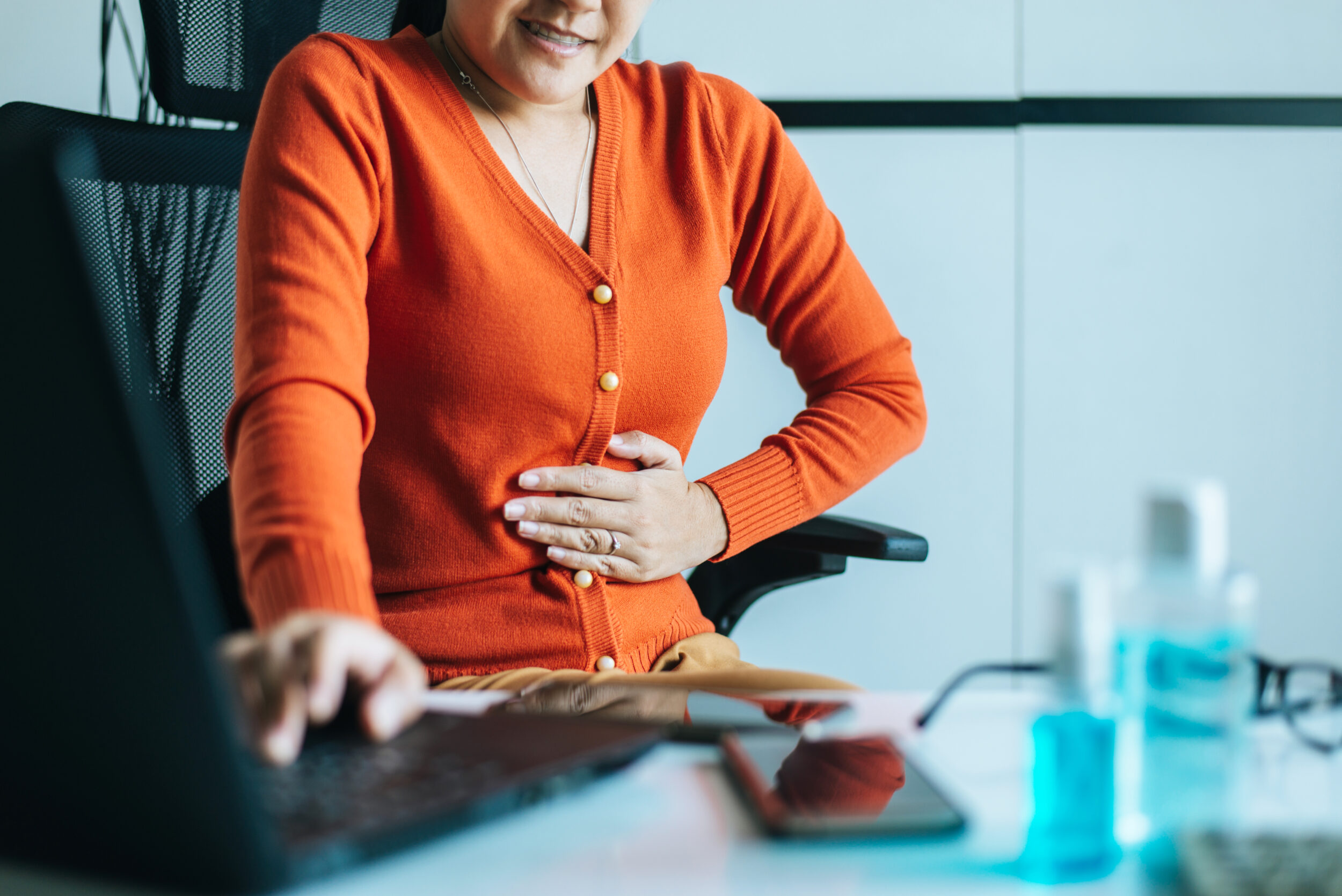 Woman sitting behind a desk and clutching stomach in pain from disrupted gut health