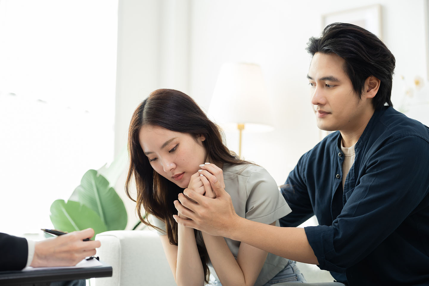 Emotional Asian woman sitting in tears while partner comforts be