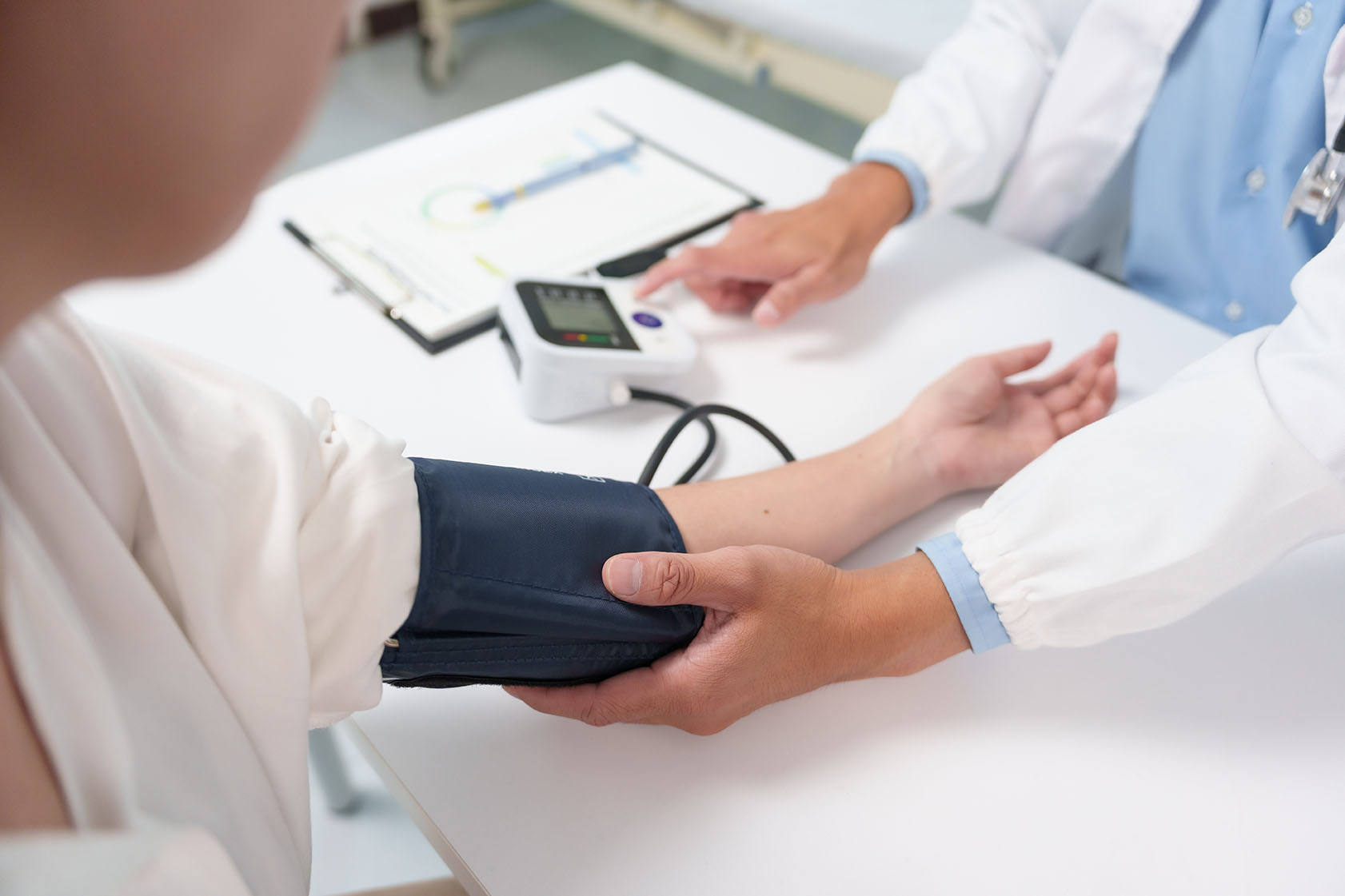 A doctor places a blood pressure cuff on a patient’s arm while pointing to a digital monitor on the desk.