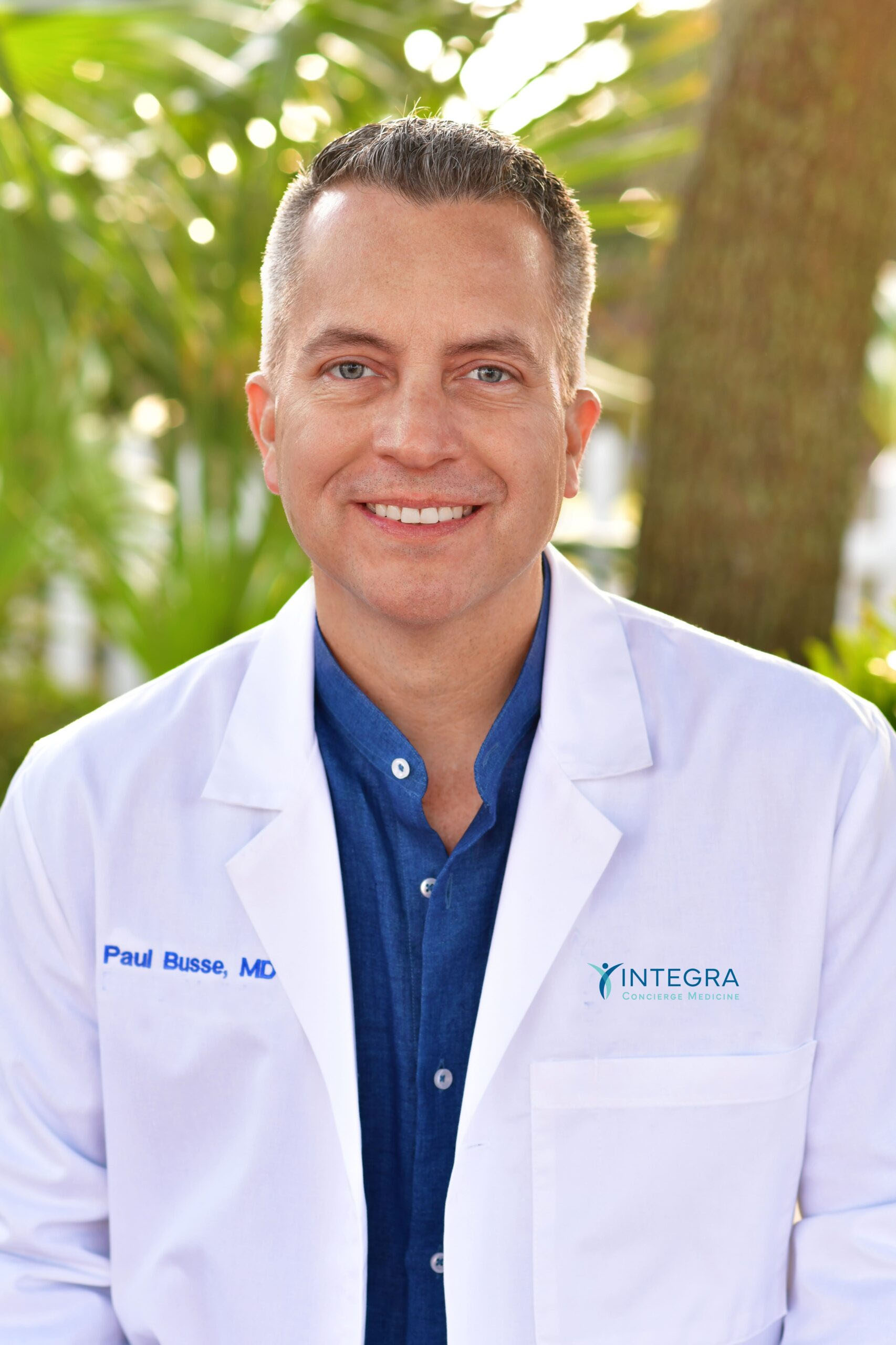 Dr. Paul Busse wearing a white coat standing outdoors with greenery in the background
