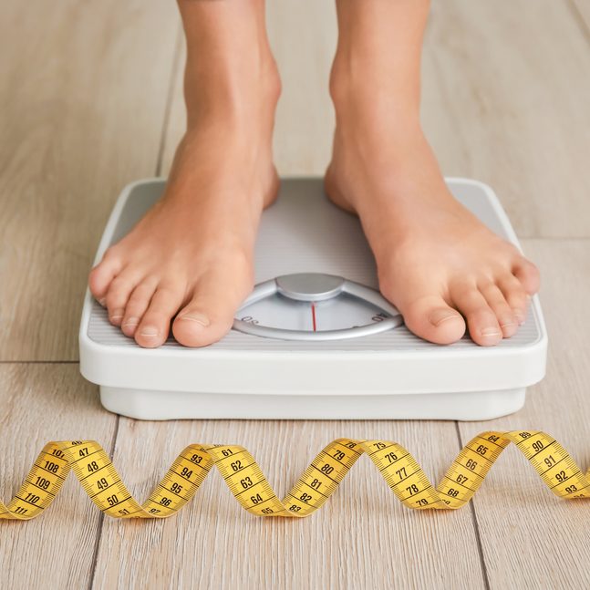 A close-up shot of a woman standing on a scale with a tape measure in front of her A close-up shot of a woman standing on a scale with a tape measure in front of her